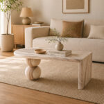 A serene and minimalist indoor living room decorated in Japandi style, featuring a beige sofa, woven rug, a unique carved light wood coffee table with sphere legs, and large potted plants