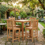 Solid teak outdoor bar table and stools set arranged in a lush courtyard garden cafe with fairy string lights