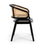 A side profile view of the Nara Teak Rattan Wave Chair in a black finish, shown from the left. This perspective emphasizes the dramatic, smooth curve of the backrest that wraps around to form the armrests, and the texture of the cane panels