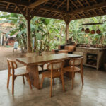 Artisan solid Suar wood dining table with teak wood dining chairs and woven rattan backrests in a semi-outdoor dining area
