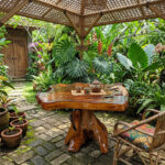 Dhifa teak root pedestal side table in a lush garden setting