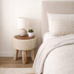 Log Slice Suar Wood Stool used as a natural wood bedside table beside a neutral upholstered bed