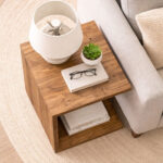 Modern solid teak side table with lower shelf beside contemporary sofa