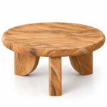 Three-quarter view of the Trivana solid Suar wood coffee table showing its natural grain, round top, and three sculptural legs